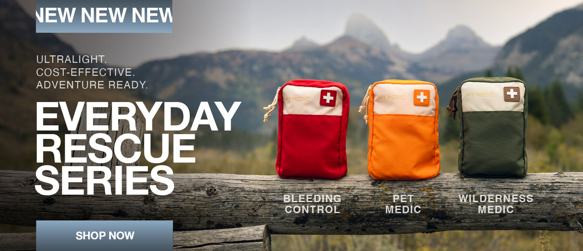 Three small first aid pouches displayed outdoors on a wooden railing with mountains in the background. The pouches are labeled Bleeding Control in red, Pet Medic in orange, and Wilderness Medic in olive green, with white medical cross patches on the front.