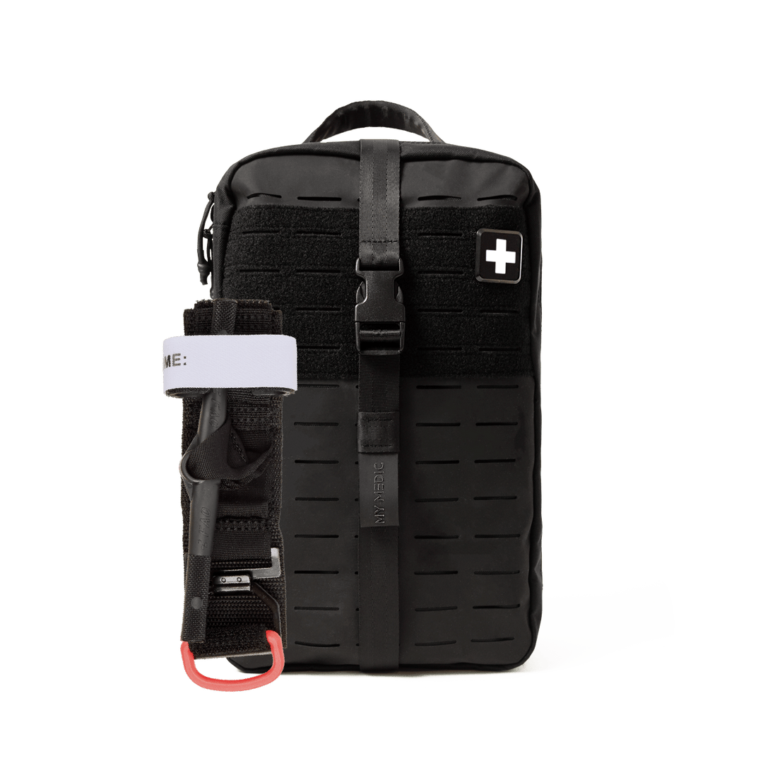 A black tactical first aid pouch with a vertical buckle strap, a side pocket holding a black tourniquet with a white band, and a white cross patch on the front, shown against a plain white background.