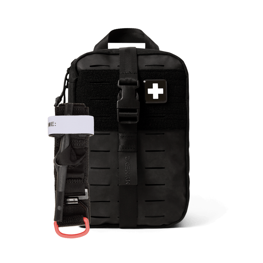 A black tactical first aid kit pouch with a front buckle strap and a white cross patch, shown on a clean white background. A black tourniquet